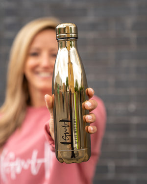 Girls Who Lift water bottle co-branded with Chillli's - shiny gold. Held by Abi Hardy.